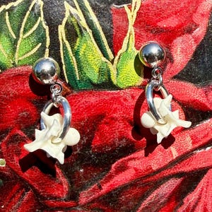 May include: A pair of silver-tone stud earrings featuring a polished spherical top and a dangling silver-tone hoop. Each hoop holds a small, off-white, organic-shaped bone-like element with multiple pointed protrusions, creating a unique dangle design.
