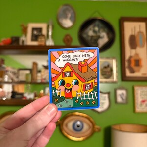 May include: A colorful sticker featuring a cartoon house with a smiling face, a red door, and a chimney. The house is yellow with a brown roof and a blue border. Text in a speech bubble reads, "COME BACK WITH A WARRANT!"