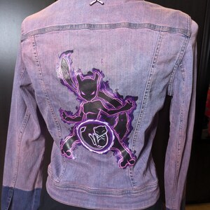 May include: A purple denim jacket with a black and purple graphic of a Pokemon character on the back. The character is surrounded by a glowing circle.