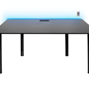 May include: A black rectangular desk with four black legs. The desk has a built-in recessed area and a blue LED light strip along the top edge. A remote control is visible on the right side.