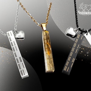 May include: Three necklaces with pendants. One is silver with a heart and a rectangular pendant with horizontal lines. Another is gold with a rectangular pendant. The third is black with a heart and a rectangular pendant with horizontal lines.