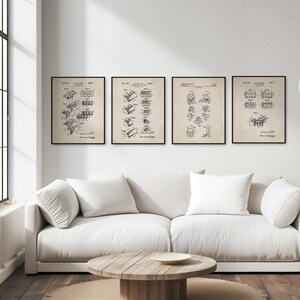 Op de afbeelding: Vier zwart-witte vintage patentprints van bouwstenen, getoond op een witte muur boven een witte bank met drie witte kussens. De prints zijn ingelijst met zwarte lijsten.