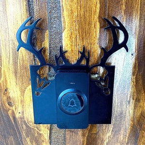 Può includere: Un campanello nero con un design a forma di corna di cervo. Il campanello è montato su una superficie in legno.