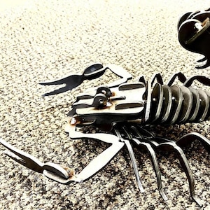 Peut inclure: Une sculpture en métal d'un scorpion avec un corps segmenté et une queue enroulée. La sculpture est faite de plusieurs morceaux de métal soudés ensemble.