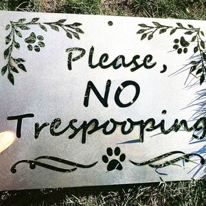 Può includere: Un cartello in metallo con sfondo bianco e lettere nere che recita "Please, NO Trespooping". Il cartello è decorato con impronte di zampe e viti di foglie.