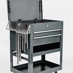 Può includere: Carrello portautensili in metallo grigio con coperchio aperto, due cassetti e un ripiano inferiore. Il carrello ha un set di utensili appesi lateralmente ed è su ruote. Il coperchio è aperto, rivelando spazio di archiviazione.