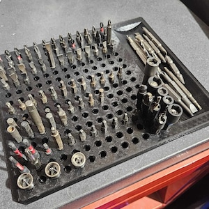 Op de afbeelding: Een zwarte plastic organizer met een raster van gaten om verschillende maten schroevendraaierbits in te bewaren. De organizer heeft een gedeelte aan de zijkant om langere bits op te bergen.