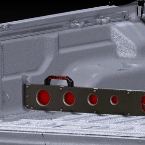 Könnte beinhalten: Ein dunkelgrauer Metall-LKW-Bettteiler mit einem schwarz-roten Griff. Der Teiler hat mehrere kreisförmige Aussparungen mit roten Akzenten. Das LKW-Bett ist ebenfalls dunkelgrau.