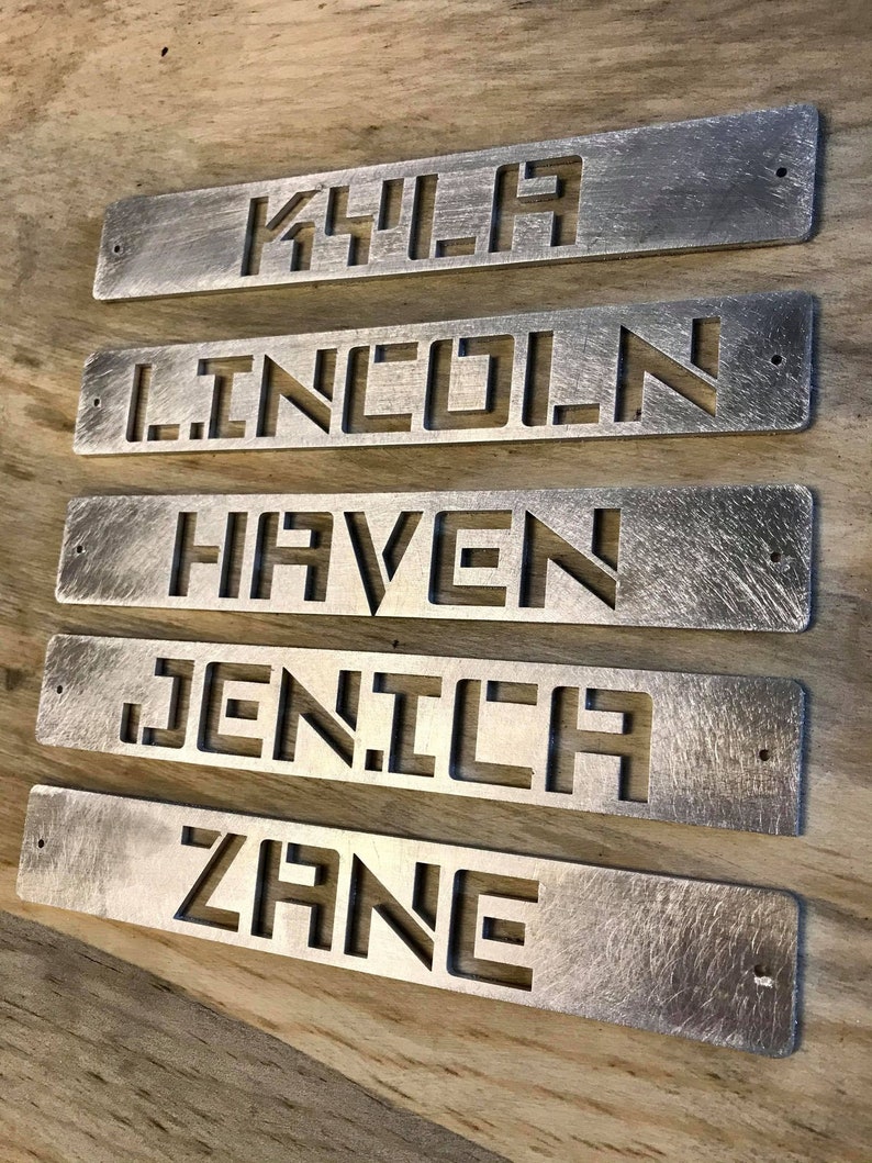May include: Five silver metal nameplates with names cut out. The names are: Kyla, Lincoln, Haven, Jenica, and Zane.