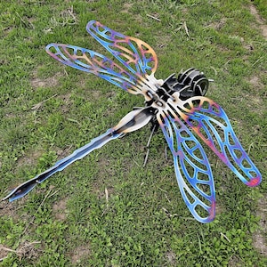 May include: A metal dragonfly sculpture with iridescent blue, purple, and orange wings. The dragonfly is made of metal and has a detailed design.