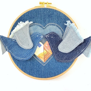 May include: A denim heart-shaped embroidery hoop with two blue denim birds perched on the edge. The birds are facing each other and have their beaks touching. The heart is filled with a folded piece of fabric.