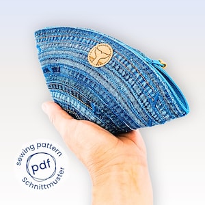 May include: A blue denim pouch with a curved shape and a blue zipper. The pouch has a wooden whale tail emblem and is held in a hand. The text "sewing pattern PDF Schnittmuster" is in a circle on the lower left.