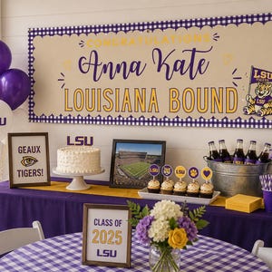 May include: A party banner with purple and white gingham borders, featuring the text "CONGRATULATIONS Anna Kate LOUISIANA BOUND" in purple and gold, alongside an LSU tiger mascot graphic, displayed above a table with themed decorations.