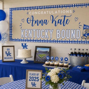 May include: A large rectangular banner with a blue gingham border, beige centre, and blue text reading CONGRATULATIONS Anna Kate KENTUCKY BOUND. The banner features a Kentucky Wildcats mascot graphic and is displayed above a party table.