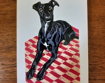 May include: A black and white dog with short fur is lying on a red and white checkered blanket. The dog has a white spot on its chest.