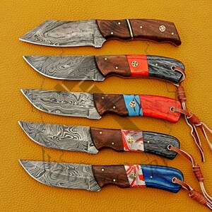 May include: Five Damascus steel knives with wooden handles and colorful epoxy resin accents. The handles feature a mix of red, blue, and white colors. The knives have a unique, wavy pattern on the blades.