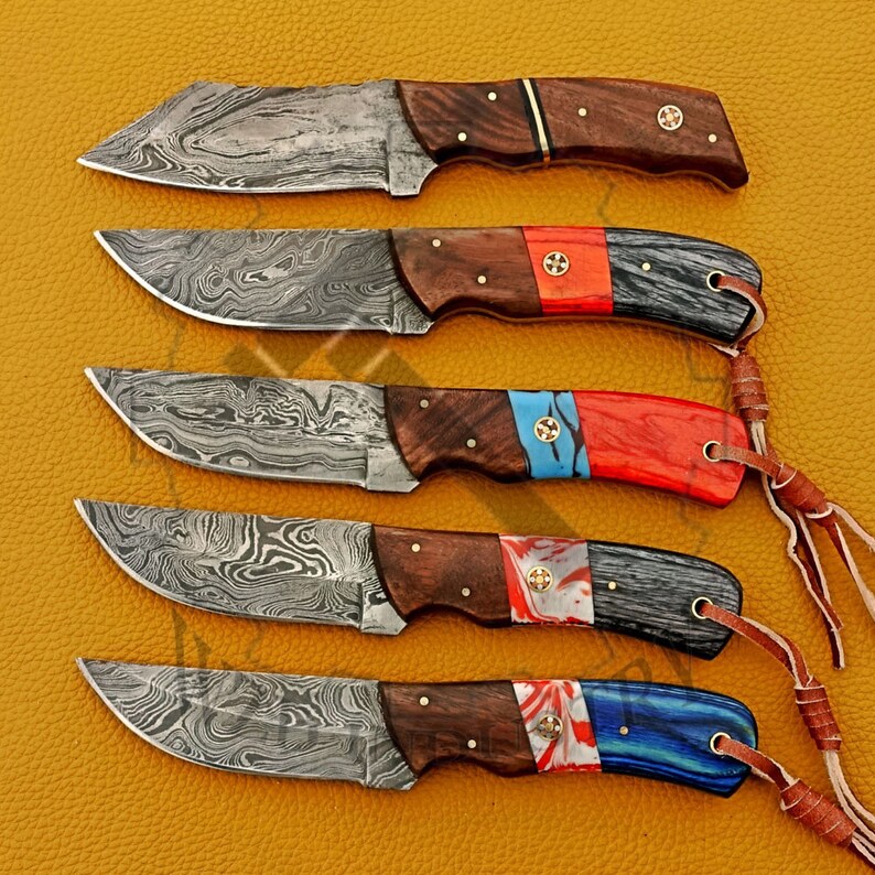 May include: Five Damascus steel knives with wooden handles and colorful epoxy resin accents. The handles feature a mix of red, blue, and white colors. The knives have a unique, wavy pattern on the blades.