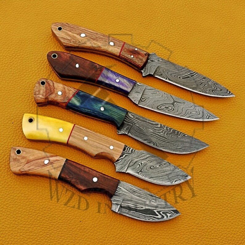 May include: Five different handmade knives with Damascus steel blades and wooden handles. Each handle has a unique combination of colors and patterns.