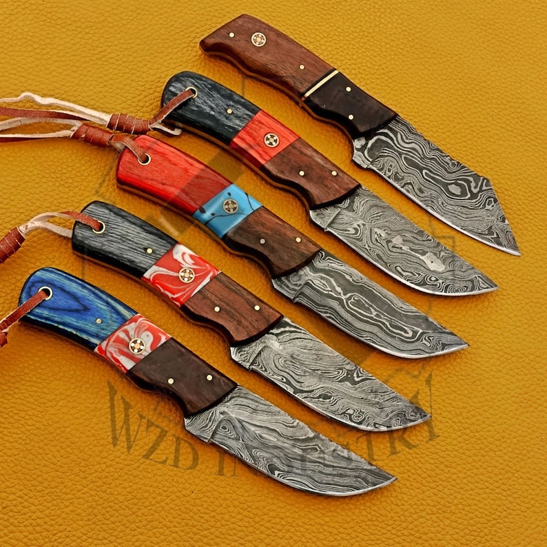 May include: Set of six Damascus steel knives with colorful wooden handles. Each knife has a different colored handle, including red, blue, and black. The blades are made of Damascus steel, which is a type of steel that is known for its beauty and durability.
