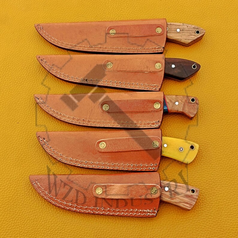 May include: Five leather sheaths with knives inside. The sheaths are brown and have stitching around the edges. The knives have wooden handles and different colored blades.