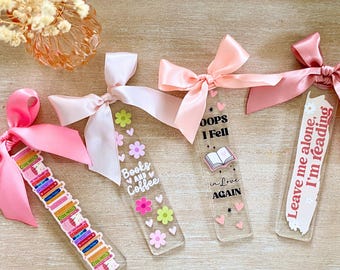 May include: Four clear acrylic bookmarks with pink ribbon bows. One bookmark has a stack of books design, another says "Books and Coffee", a third says "Oops I Fell in Love Again", and the last says "Leave me alone, I'm reading".