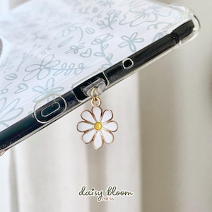 Peut inclure: Une coque de téléphone transparente avec un fond blanc et un motif floral bleu clair. Une chaîne dorée avec un charme de marguerite blanche pend du bas de la coque. Le texte "daisy bloom press" est imprimé au bas de la coque.
