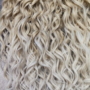 May include: A set of blonde and white ombre curly dreadlocks. The dreadlocks are tied together at the top.