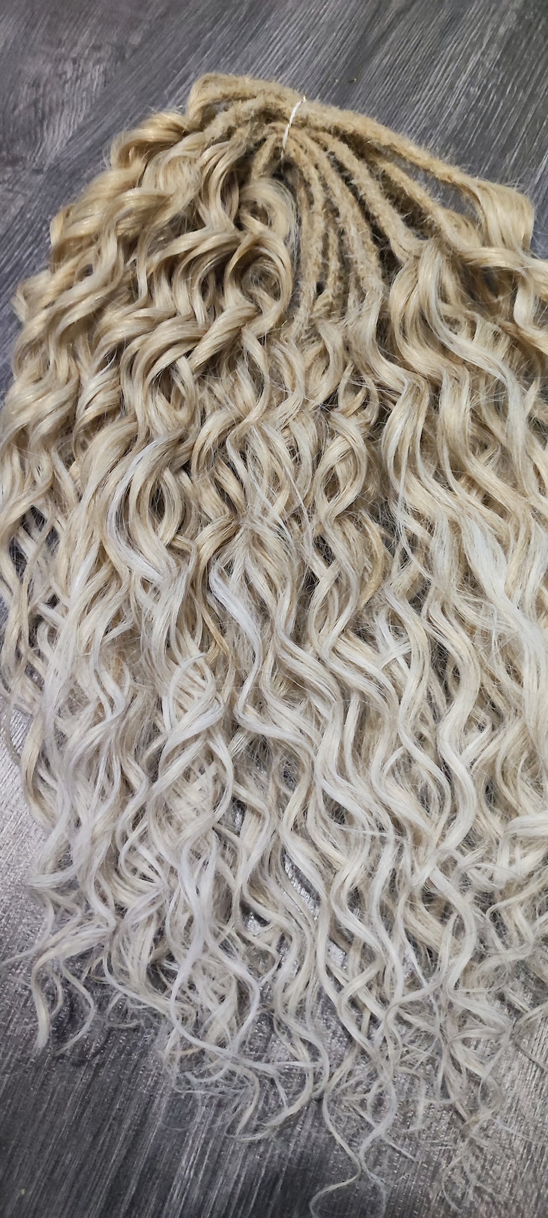 May include: A set of blonde and white ombre curly dreadlocks. The dreadlocks are tied together at the top.