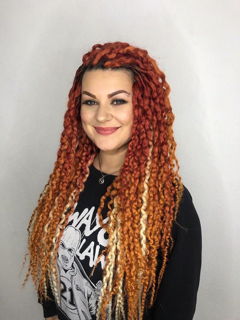 May include: A woman with long, thick braids in shades of orange, red, and blonde. She is wearing a black shirt with a white graphic print that says "WAG" and "LAW".