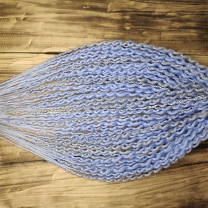 May include: A bundle of blue and gray synthetic dreadlocks with a wavy texture. The dreadlocks are tied together at one end with a natural-colored string. The background is a wooden surface.