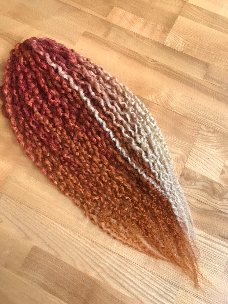 May include: A long strand of ombre hair extensions with a red, orange, and blonde color gradient. The hair is in a curly style.