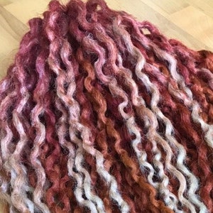 May include: A close-up of a bundle of curly, hand-spun yarn in shades of white, brown, and red.