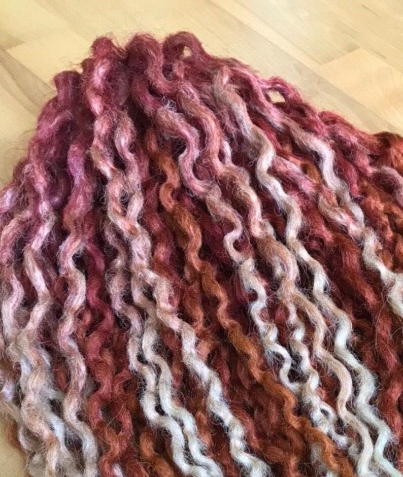 May include: A close-up of a bundle of curly, hand-spun yarn in shades of white, brown, and red.
