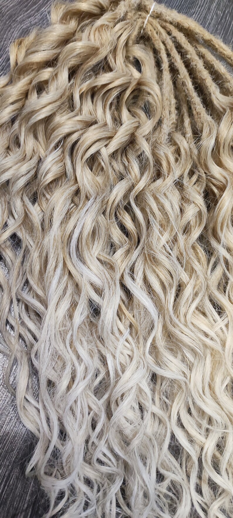 May include: A bundle of blonde and light blonde curly synthetic dreadlocks. The dreadlocks are tied together with a white string.