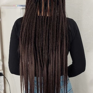 May include: A person with long, dark brown dreadlocks. The dreadlocks are styled in a straight, even pattern and fall to the person's waist. The person is wearing a black long-sleeved shirt and blue jeans.