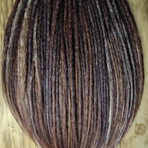 Op de afbeelding: Een set bruine, paarse en witte synthetische dreadlocks. De dreadlocks zijn lang en recht en zijn gerangschikt in een nette, gelijkmatige rij.