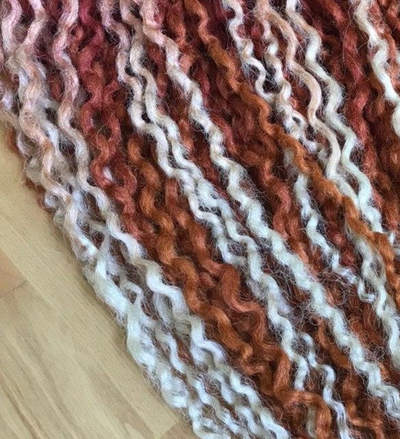 May include: Close-up of a bundle of curly yarn in shades of white and orange-red. The yarn is arranged in rows, creating a textured and colorful pattern.