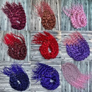 May include: A collection of nine bundles of curly hair extensions in various colors, including red, pink, purple, and blue. The hair is arranged in a grid pattern on a wooden surface.