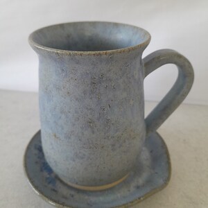 May include: A blue ceramic mug with a matching saucer. The mug has a speckled glaze and a rounded shape. The saucer is slightly smaller than the mug and has a similar speckled glaze.