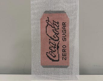 May include: Needlepoint canvas featuring a pink Coca-Cola Zero Sugar can design. The can has black lettering and a gray top and bottom. The canvas is white and rectangular, perfect for a DIY project or a unique piece of art.