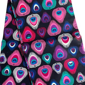 May include: A dark navy fabric featuring a repeating pattern of stylized peacock feathers. The feathers are rendered in vibrant shades of pink, purple, teal, and white, creating a bold and colorful design. The fabric is folded, showing the pattern's continuity.