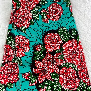 May include: A teal fabric with a red, white, and green floral print. The fabric features large roses and smaller flowers with white polka dots.