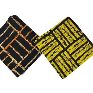 Puede incluir: Dos cuadrados de tela doblados con patrones geom&eacute;tricos. Uno es negro con l&iacute;neas naranjas y crema, el otro es amarillo con l&iacute;neas negras. La tela tiene un dise&ntilde;o gr&aacute;fico audaz, adecuado para ropa o decoraci&oacute;n del hogar.