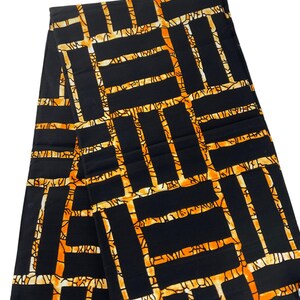 Puede incluir: Tela negra con un patr&oacute;n geom&eacute;trico en naranja y crema. El dise&ntilde;o presenta una estructura similar a una cuadr&iacute;cula con elementos rectangulares y lineales. La tela est&aacute; doblada, mostrando la repetici&oacute;n del patr&oacute;n.