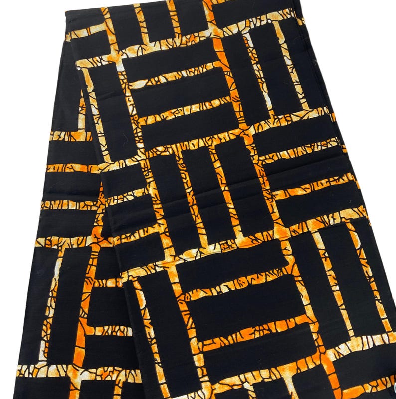 Puede incluir: Tela negra con un patr&oacute;n geom&eacute;trico en naranja y crema. El dise&ntilde;o presenta una estructura similar a una cuadr&iacute;cula con elementos rectangulares y lineales. La tela est&aacute; doblada, mostrando la repetici&oacute;n del patr&oacute;n.