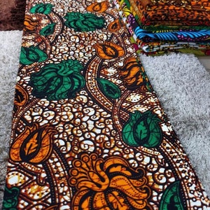 May include: A colorful fabric with a repeating pattern of green, orange, and brown flowers on a white background. The fabric has a traditional African design.