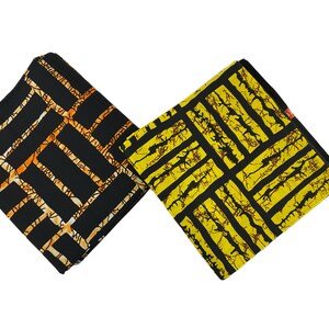 Puede incluir: Dos cuadrados de tela doblados con patrones geom&eacute;tricos. Uno es negro con l&iacute;neas naranjas y crema, el otro es amarillo con l&iacute;neas negras. Las telas tienen un dise&ntilde;o rectangular repetitivo, adecuado para proyectos de costura o artesan&iacute;a.