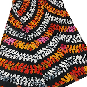 May include: A folded piece of fabric featuring a black background with a repeating pattern of wavy, diagonal stripes. The stripes consist of stylized leaf or fern motifs in vibrant shades of orange, yellow, pink, and white with a textured appearance.
