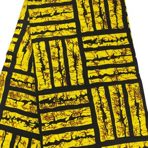 Puede incluir: Una tela doblada con un patr&oacute;n geom&eacute;trico audaz. El dise&ntilde;o presenta una cuadr&iacute;cula de rect&aacute;ngulos y l&iacute;neas negras sobre un fondo amarillo brillante. Detalles marrones de forma org&aacute;nica llenan los rect&aacute;ngulos.