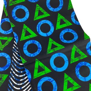 May include: Black fabric with a repeating pattern of blue circles and green triangles. The circles have a blue, tree-like design inside. A section of the fabric has white and black stripes.